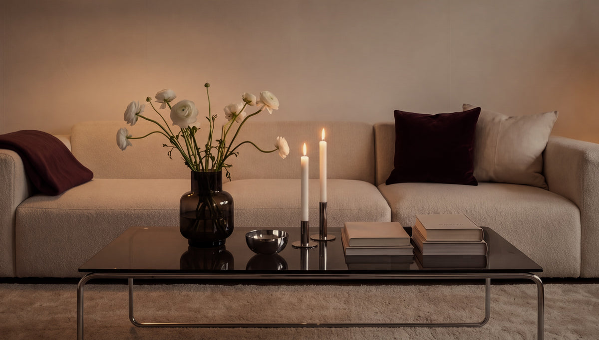 A cosy living room at dusk: cream sofa, white ranunculus and lit candles on a glass coffee table